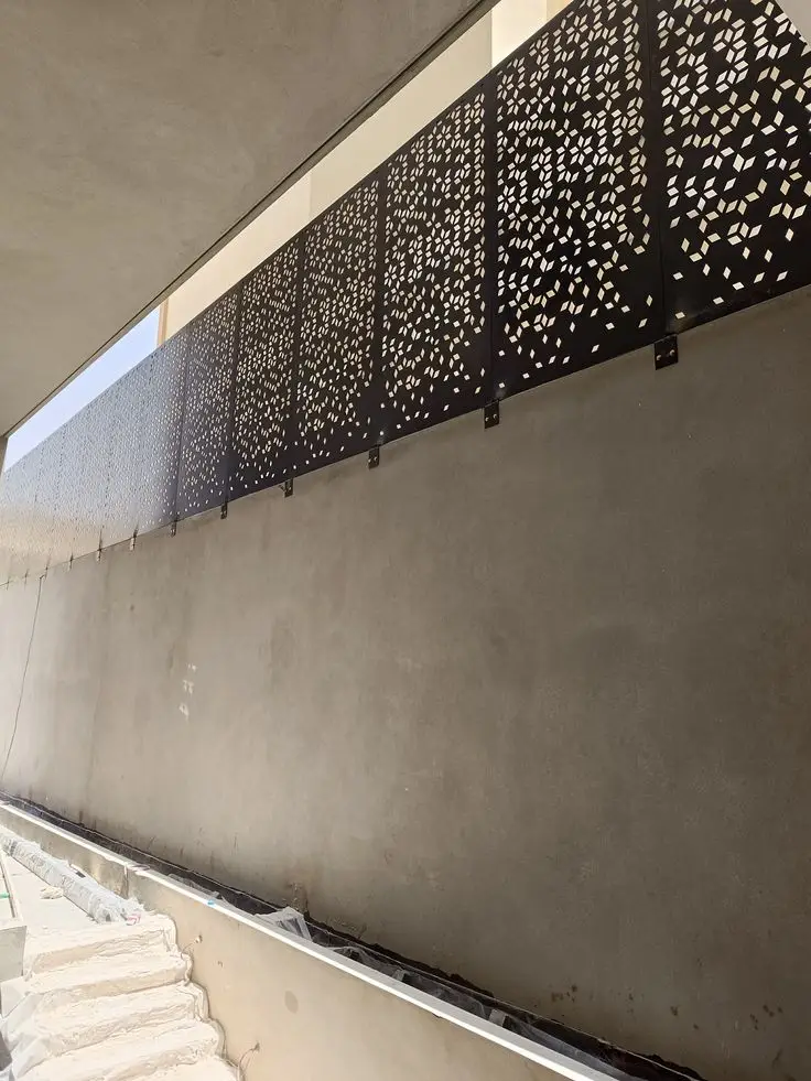 ساتر معدني داكن، مزخرف بنقوش مقصوصة بالليزر، ومثبت على جدار خرساني.