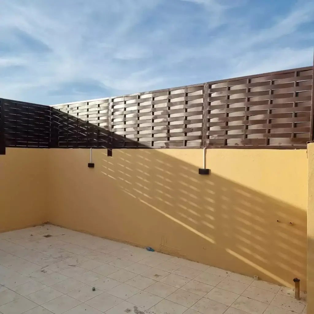 ساتر حديد مجدول باللون البني الداكن مثبت على سور خارجي لمنزل.